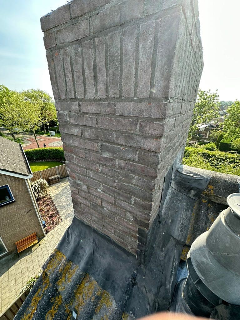 Vernieuwd plat dak van een dakkapel met bitumen dakbedekking en nette aansluiting rond een gemetselde schoorsteen.