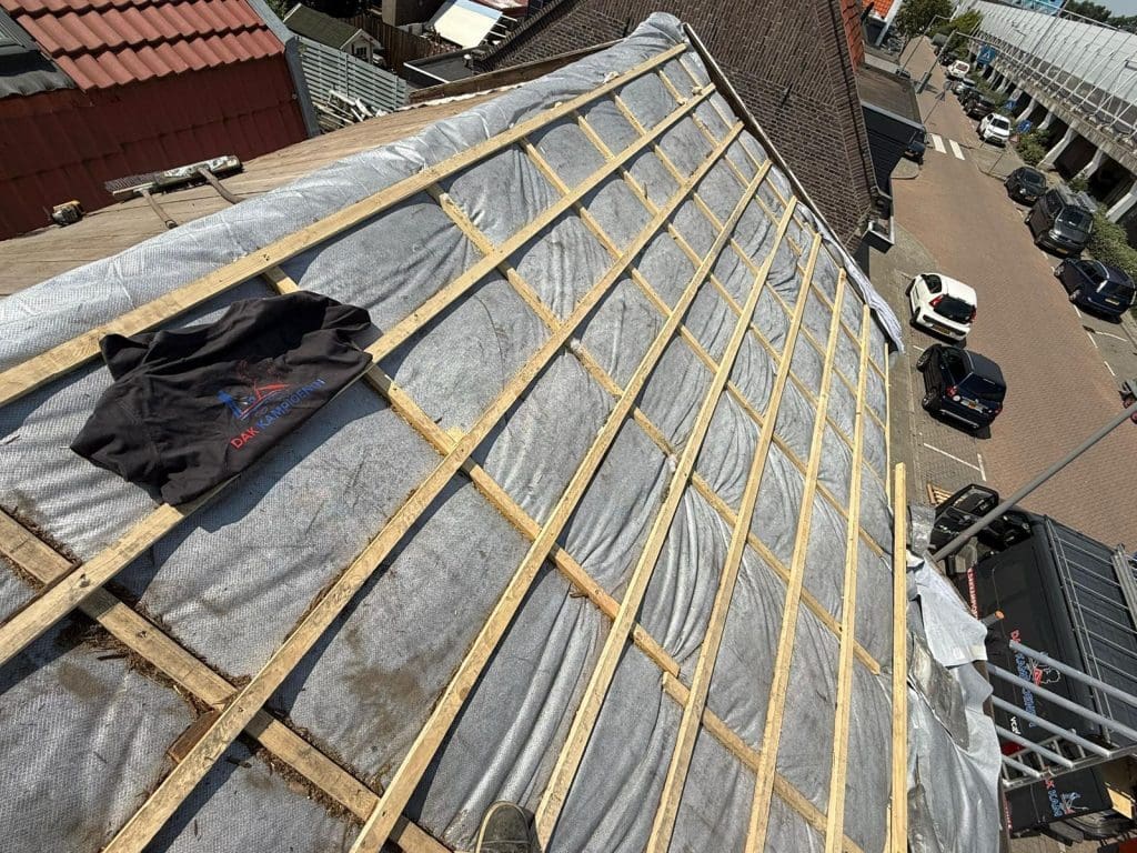 Bakstenen gebouw met een steil rood zadeldak met dakpannen, schoorsteen en bomen op de voorgrond.