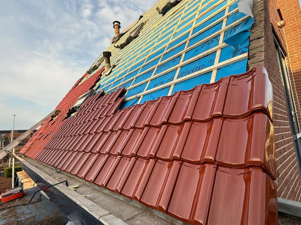 Schuin dak in renovatie met nieuwe roodbruine dakpannen, blauwe onderdakfolie en houten panlatten zichtbaar.