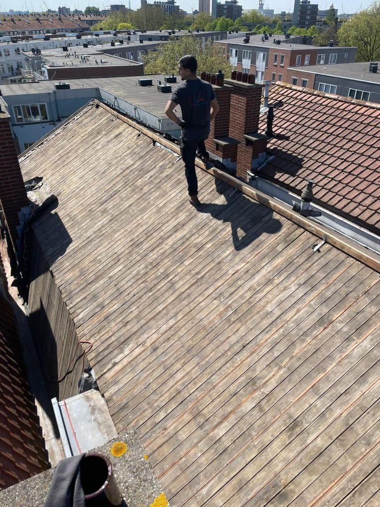 Dakdekker plaatst keramische dakpannen op een hellend pannendak rond een dakkapel met raam.