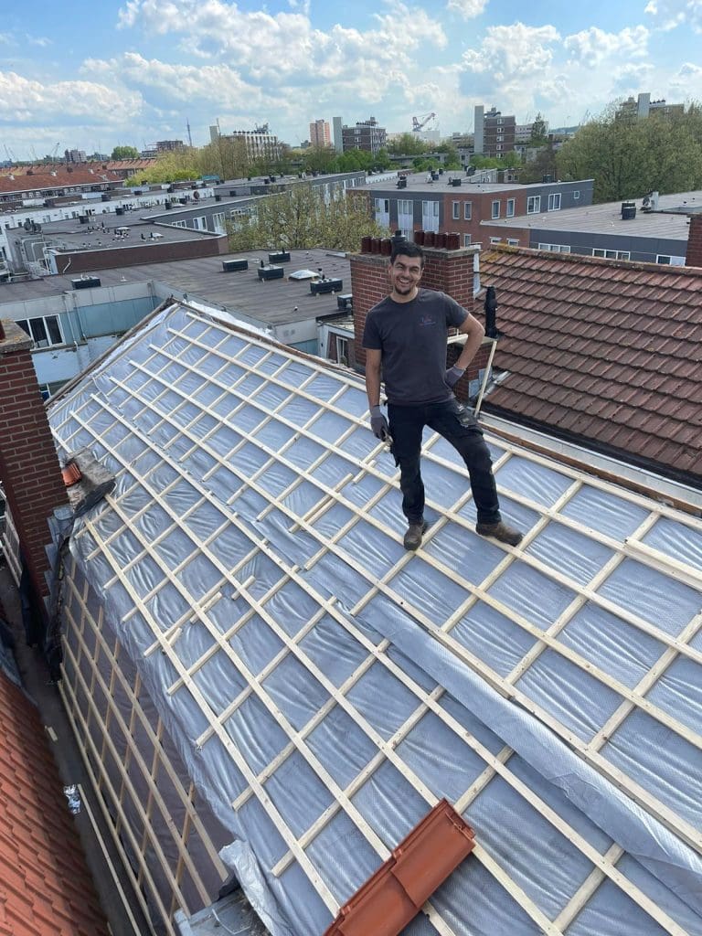 Dakdekker op een hellend pannendak in renovatie, met dakfolie, houten tengels en panlatten zichtbaar.