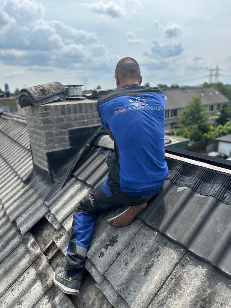 Dakdekker werkt aan de afwerking rond een schoorsteen op een schuin pannendak.