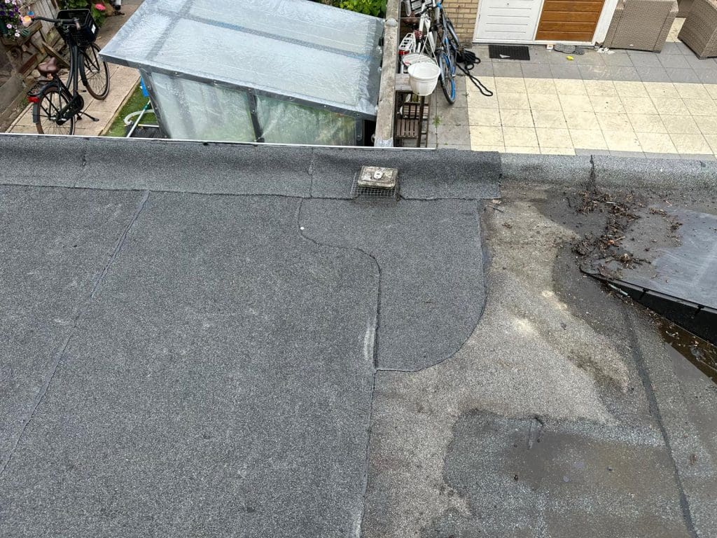 Plat dak met bitumen, dakdoorvoer en zichtbare herstelplek.