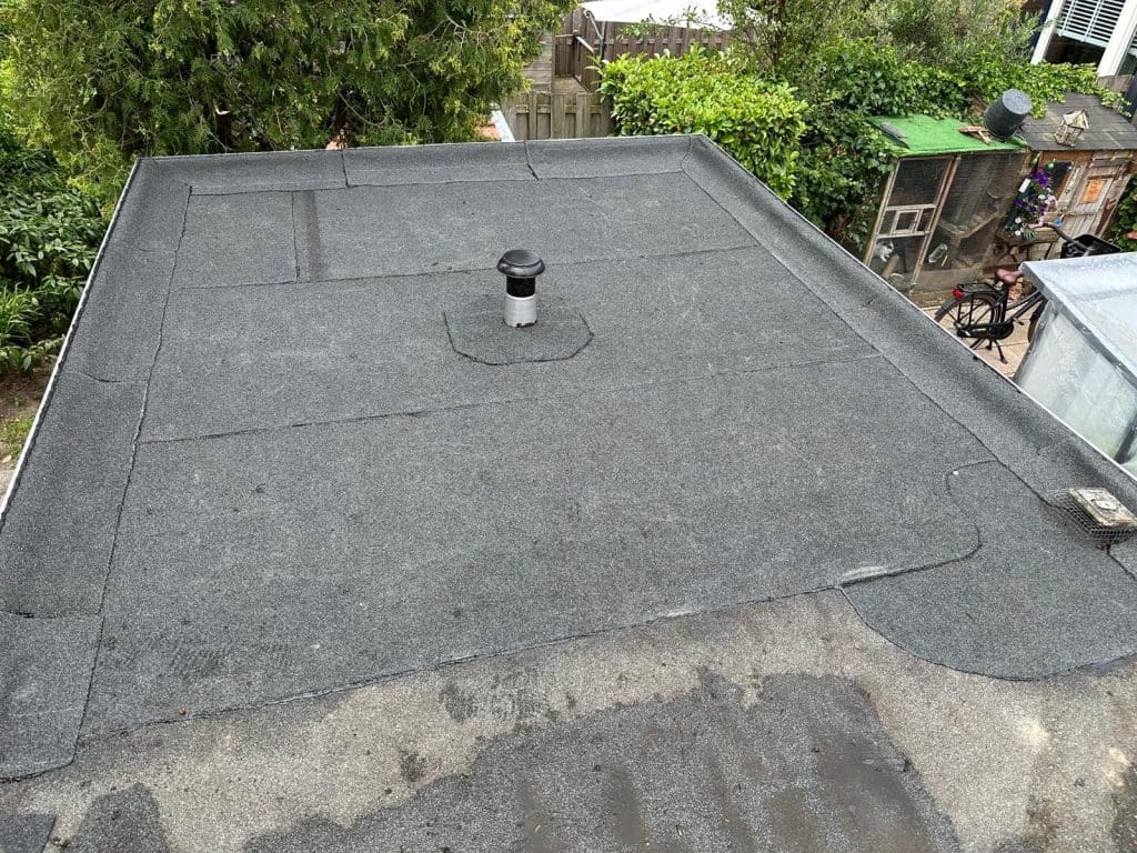 Plat dak met bitumen dakbedekking en een ventilatiepijp in het midden.