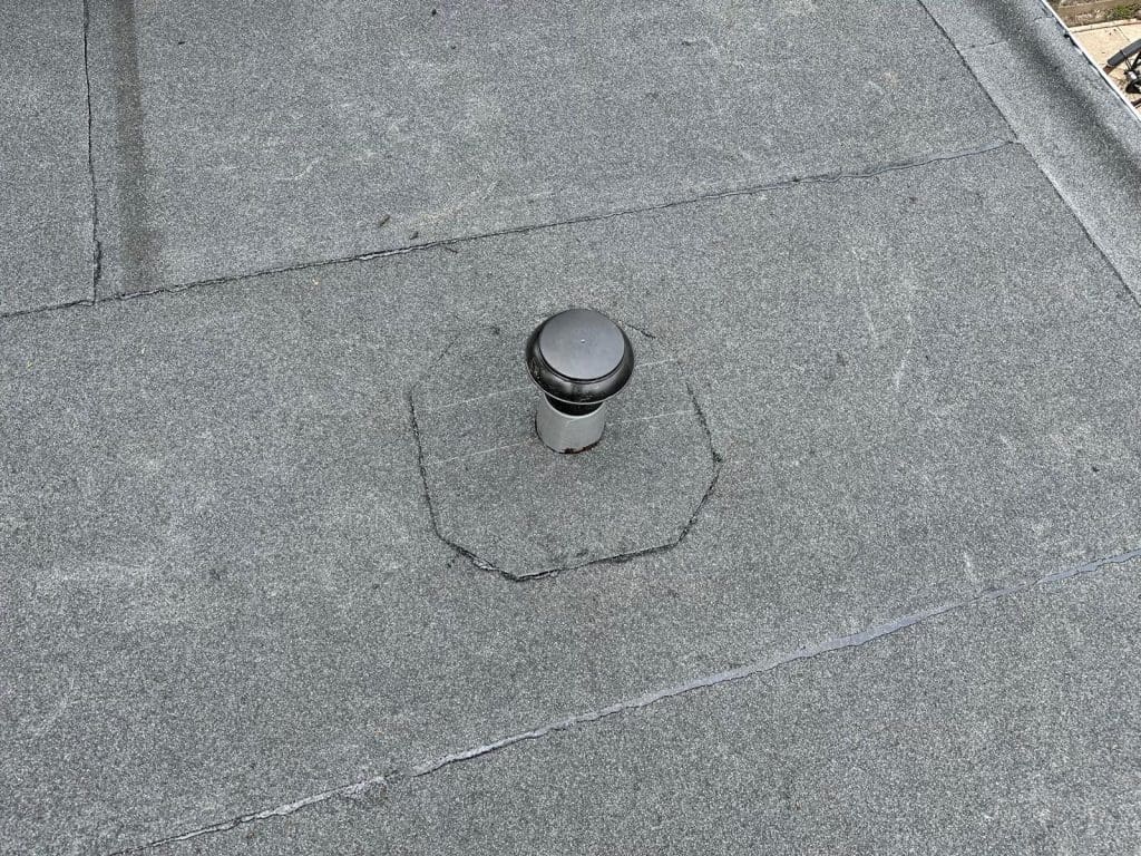 Plat dak met bitumen dakbedekking en een dakdoorvoer.