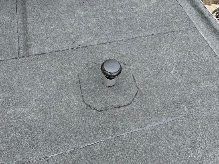Plat dak met bitumen dakbedekking en een dakdoorvoer.